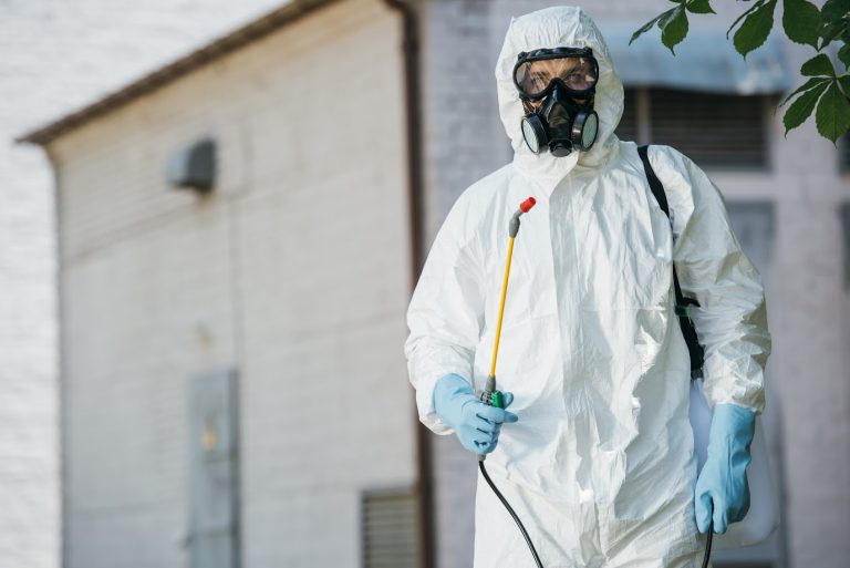 A professional pest control technician inspects the exterior of a house for signs of pest entry points.