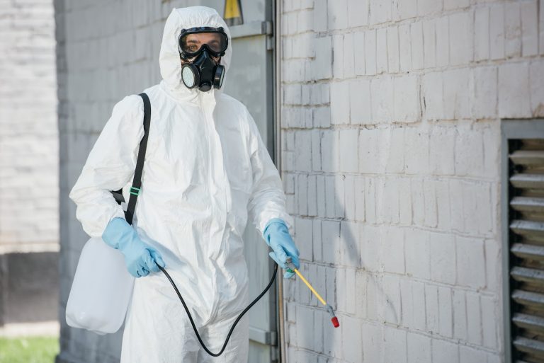 Pest control technician applying eco-friendly treatment around the foundation of a home.